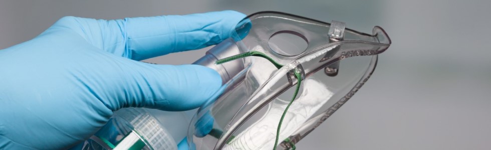 Ein Arzt mit blauen Handschuhen hält eine Sauerstoffmaske in der Hand