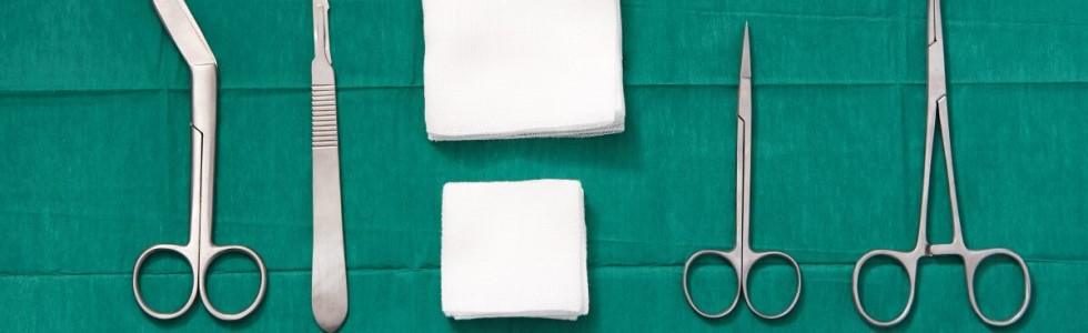 Verschiedene Einweginstrumente und Verbandmaterial auf grünem OP Tuch