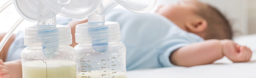 Babybedarf Ein Baby liegt neben zwei Milchpumpen – die Mutter hat Babybedarf gekauft.